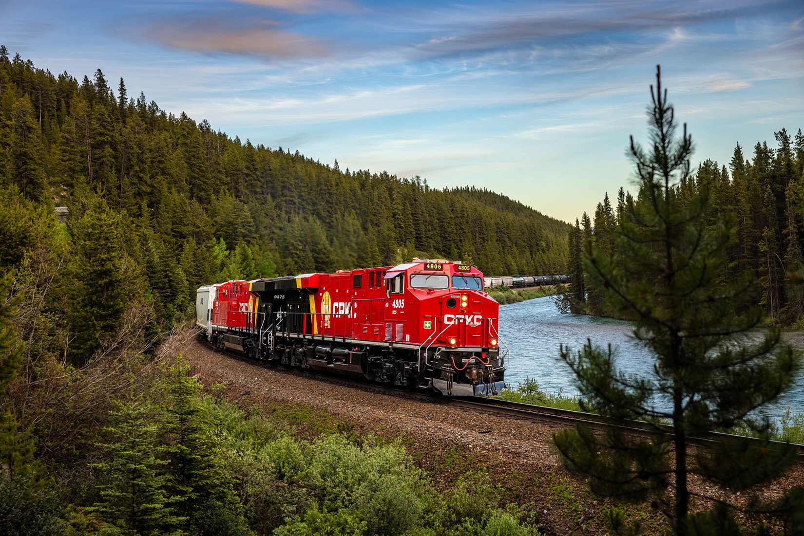 A red CPKC train engine crossing a bridge over water