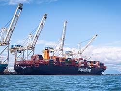 A shipping boat sitting at dock with four cranes above