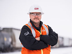 A person wearing a high visibility vest and a white hard hat standing in front of a train