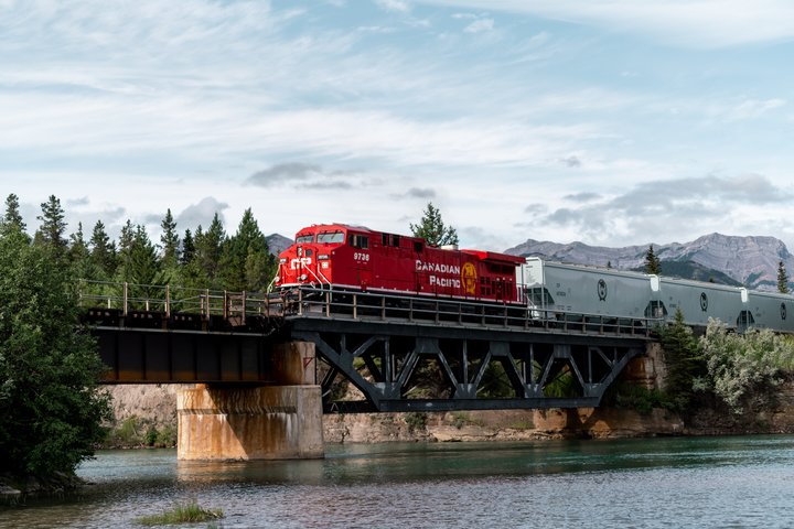 A red CPKC train engine crossing a bridge over water